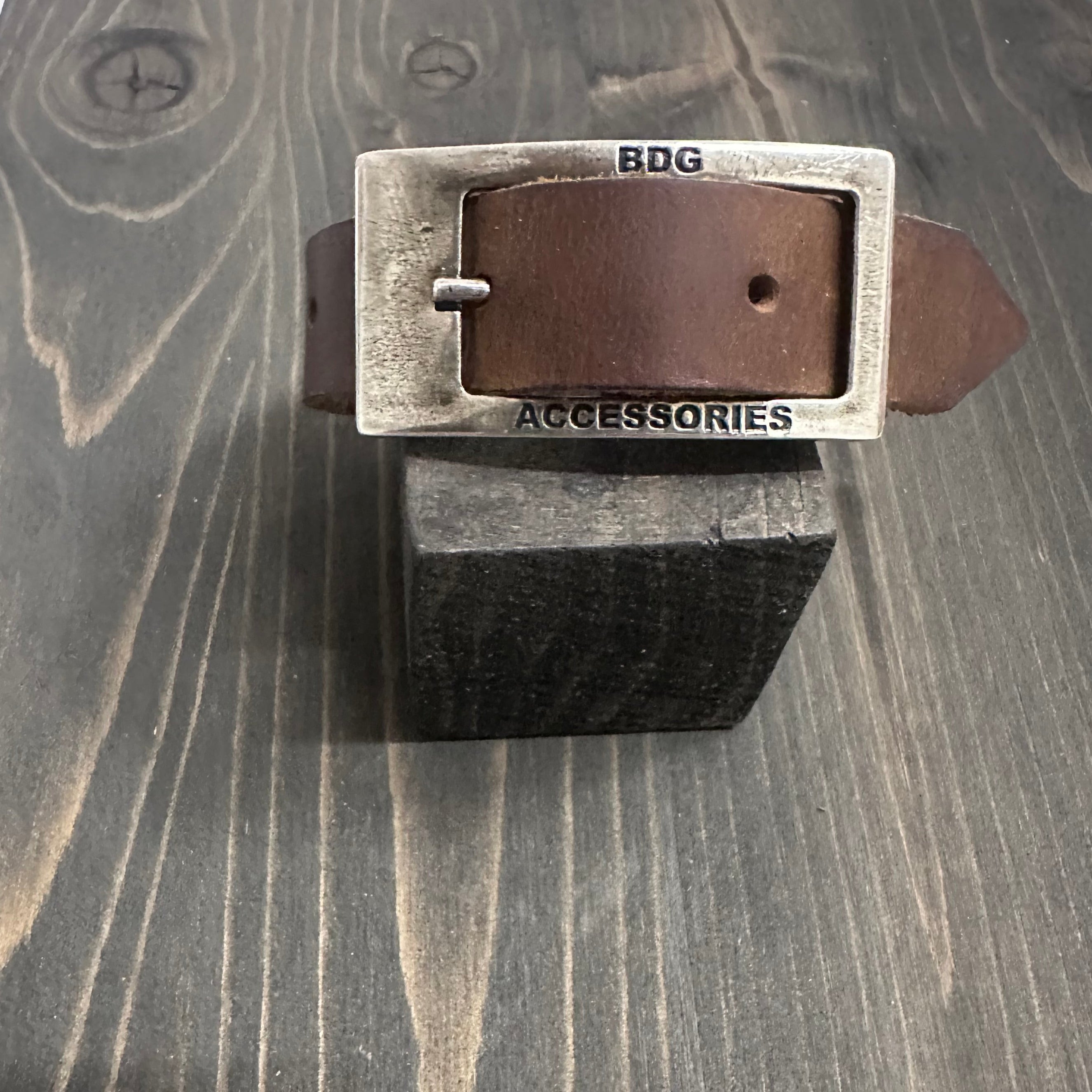 BDG Accessories leather bracelet in old style resting on a wooden block, showcasing its vintage design and craftsmanship.