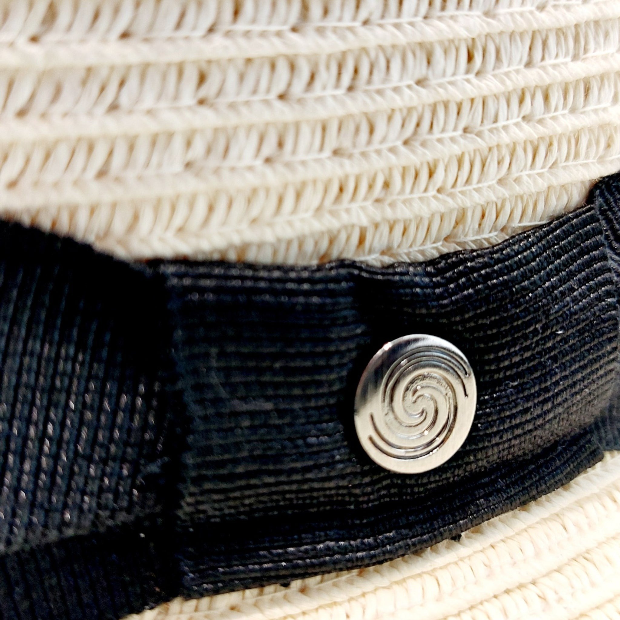 Close-up of Sbarià natural straw bombetta hat with spiral pin, metallic button, black band, and white woven straw detail.