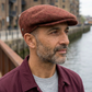 Uomo con viso rivolto a destra, camicetta bordeaux e coppola London coccio